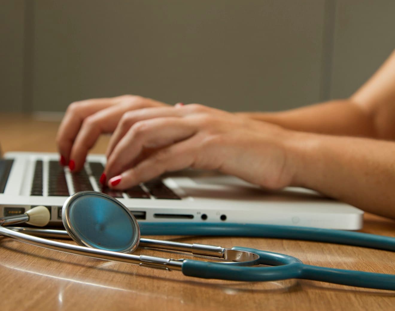 A clinician working at a laptop with a stethoscope beside them