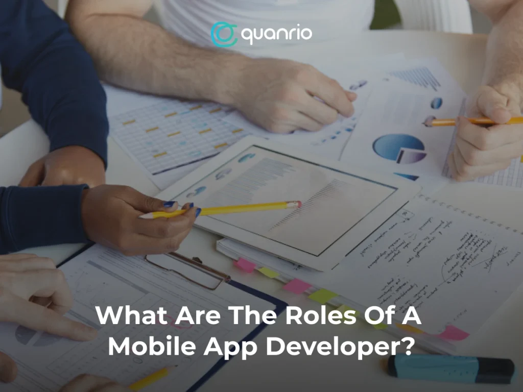 People working together on documents and charts with the text 'What Are The Roles Of A Mobile App Developer?' displayed.